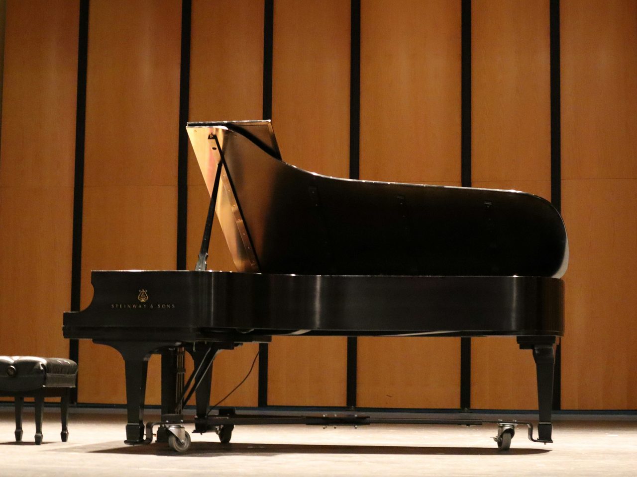 A concert grand piano with its lid raised on a recital stage, bench alongside